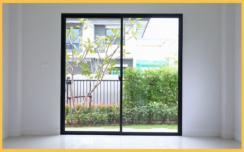 Sliding glass doors frame a view of a lush garden with greenery and a fence, brightening a minimalist interior space.