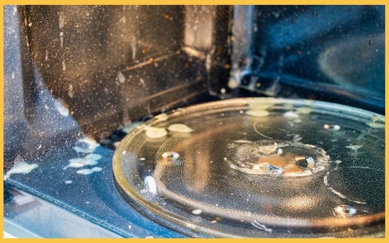 Interior of a dirty microwave with splattered food residue and a stained glass turntable plate.