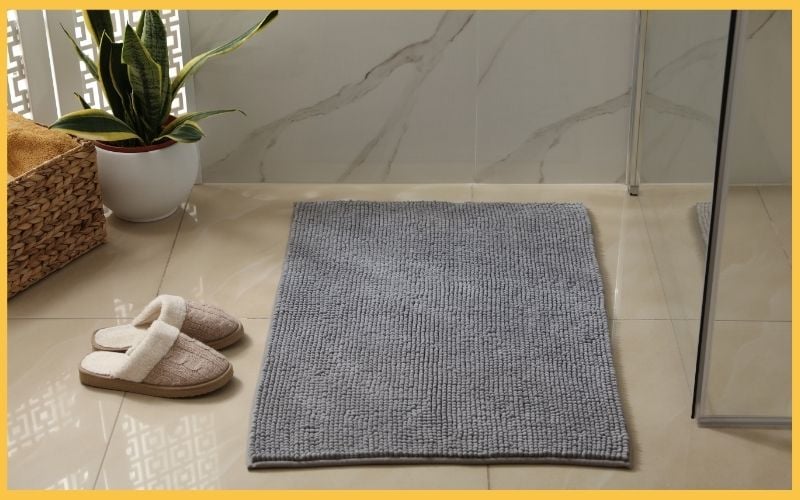 Cozy bathroom scene featuring a gray textured rug, soft slippers, a potted plant, and modern tiles.