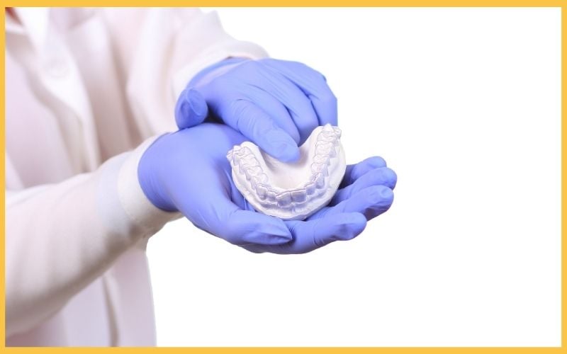 A healthcare professional in blue gloves holds a dental mold.