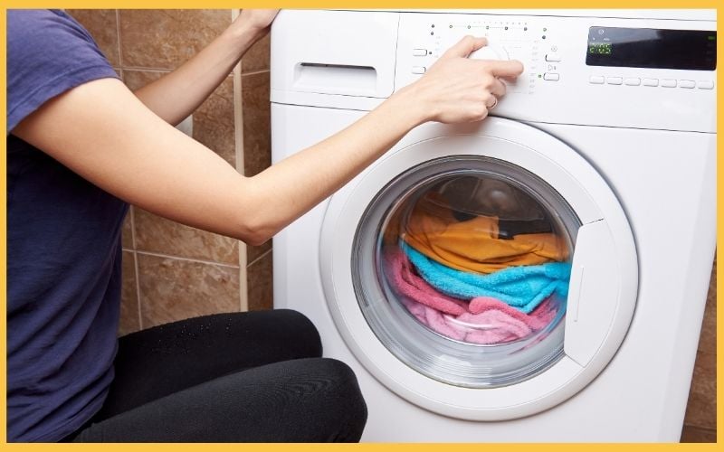 A person adjusts the settings on a front-loading washing machine with colorful towels inside the drum.