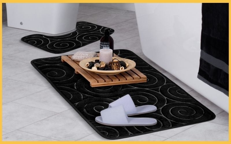 A stylish bathroom scene featuring a black spiral rug, wooden tray with decorative items, a candle, and cozy white slippers.