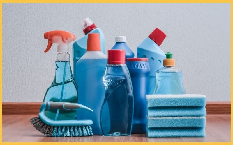 A variety of blue cleaning products and sponges arranged on a wooden surface, including spray bottles and liquid detergents.