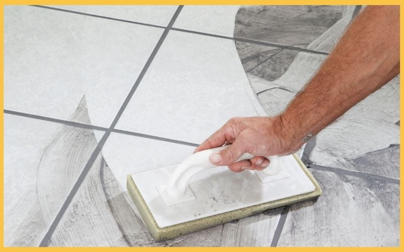 A hand uses a trowel to spread grout on large, patterned floor tiles during a renovation project.