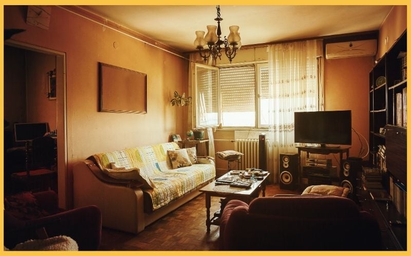 Cozy living room featuring a patterned sofa, wooden coffee table, TV stand, and bright windows adorned with sheer curtains.