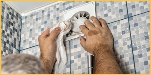 A person cleaning a dirty exhaust fan.